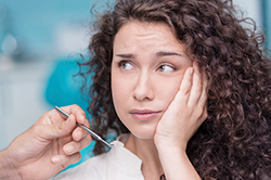 A woman holding her cheek near doctor's hand with dental tool
