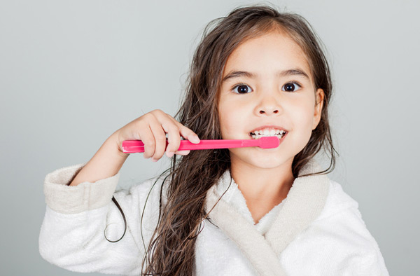 Young girl brushing her teeth with a pink toothbrush