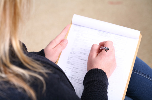 Woman filling out insurance paperwork on clipboard with pen