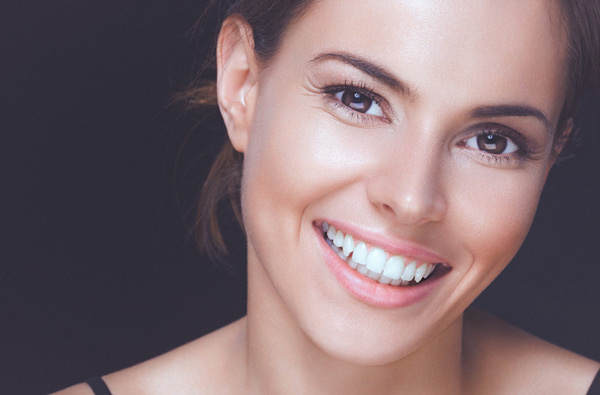 Close up of smiling woman with beautiful teeth in front of brown background
