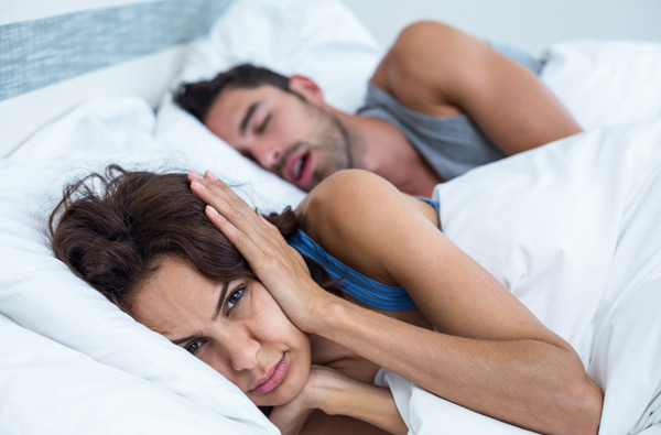 Woman covering ears while husband snores because of sleep apnea before visiting Myers Park Dental Partners in Charlotte, NC